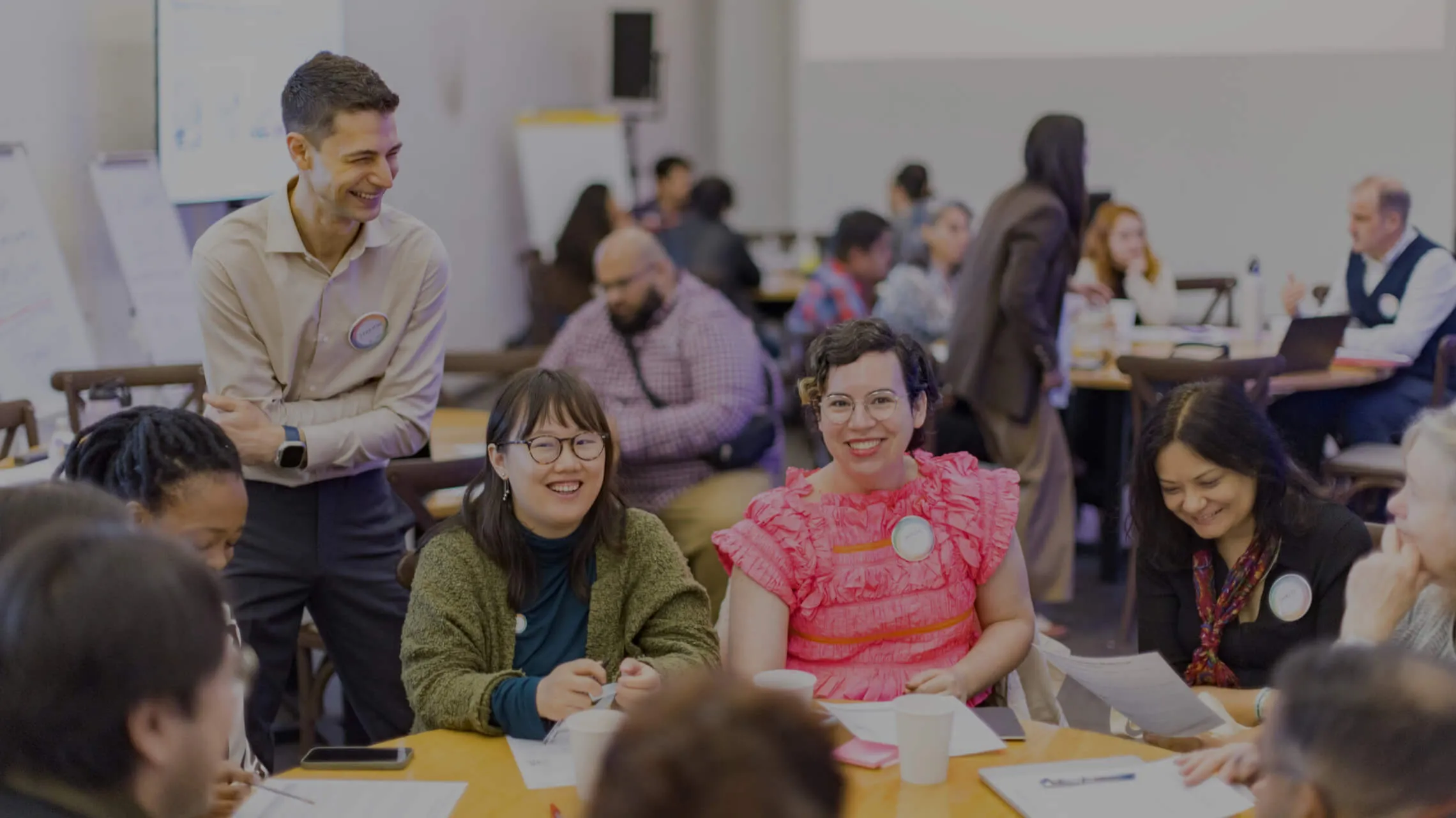 Participants seated around tables at an Interledger workshop, talking and smiling, with flip charts behind them